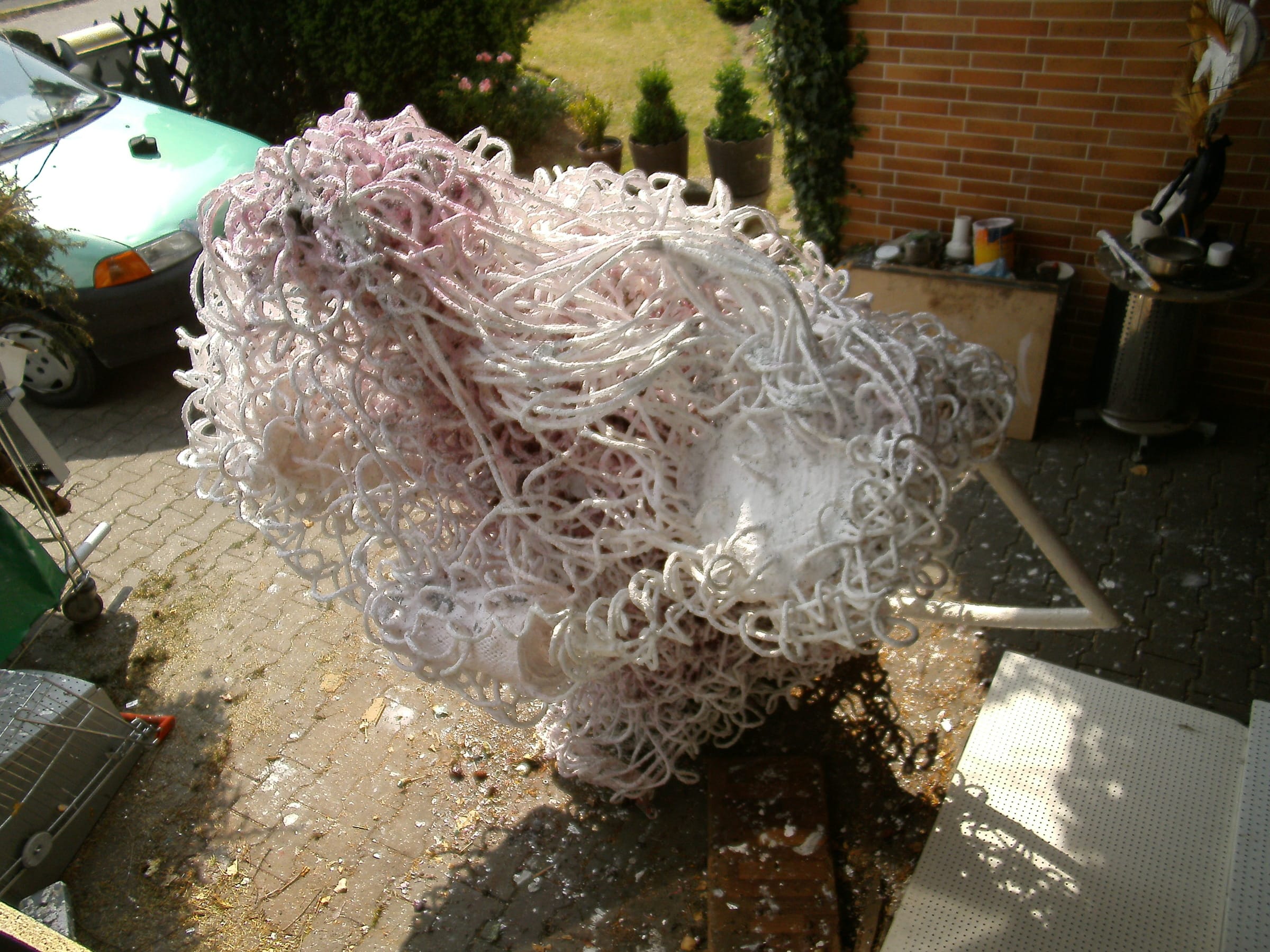 Rosa-weisse Skulptur aus Schlingen mit weissem Rohrbogen auf einem gepflasterten Hof