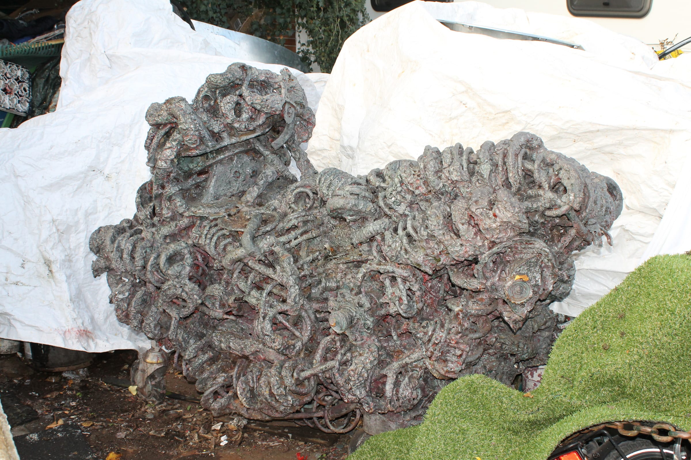 Breite grau-violette Skulptur aus Metallschlingen vor weissen Planen